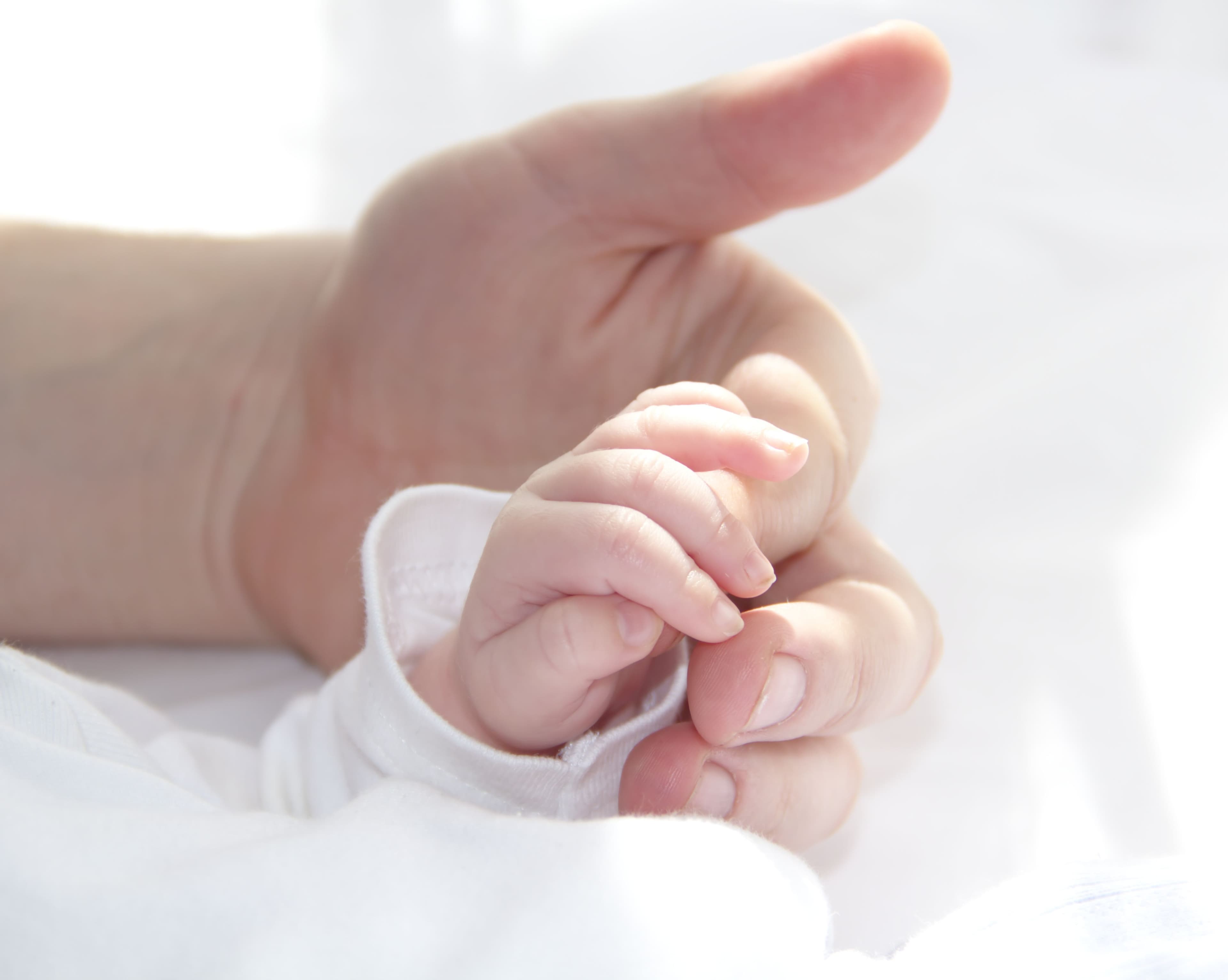 A baby holding tightly onto an adult's finger